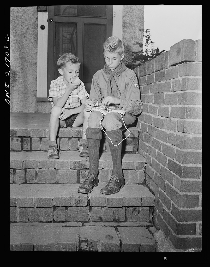 Earl Babcock watching while Howard, his brother, in his Boy Scout uniform, practices tying knots [PHOTO: Library of Congress]