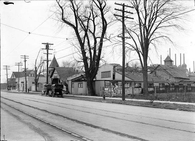 A view of Beach Avenue west of Lake Avenue. Buildings to be torn down for an automobile parking space are pictured as well as Manitou Trolley tracks in the foreground and the Charlotte blast furnace and chimney in the background. [PHOTO: Albert R. Stone]