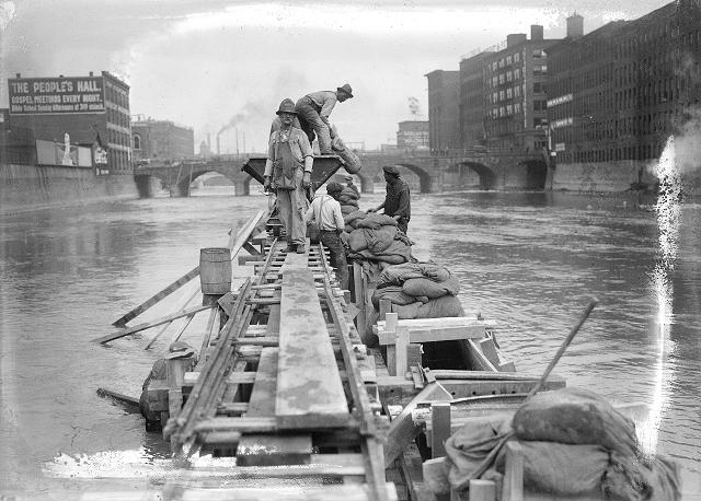 Men work from narrow wooden platforms filling concrete forms with sand bags. [PHOTO: Albert R. Stone]