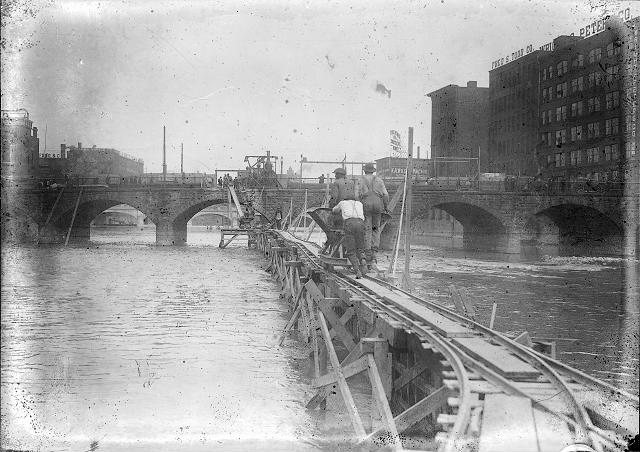 Three workmen push a hopper along a raised trestle in the middle of the Genesee River. [PHOTO: Albert R. Stone]