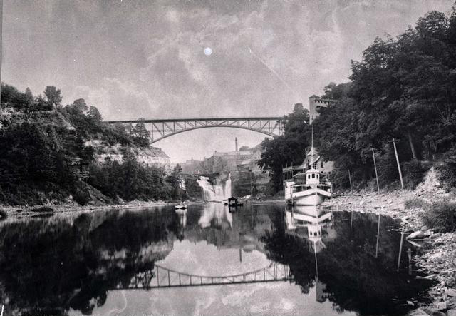 A view of the Genesee River, looking south towards Driving Park Avenue Bridge and the Lower Falls. A large boat is docked at the Glen House on the right.  [PHOTO: Rochester Public Library]