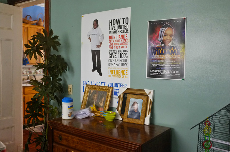 This poster in Mary's living room recognizes her community volunteer efforts. Next to Mary's poster is another in memory of her grandaughter Shawntayvia Williams. [PHOTO: Julie Gelfand]