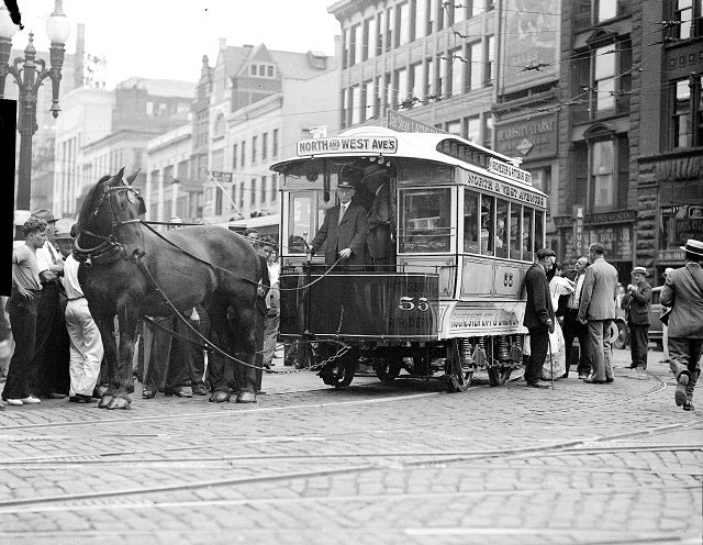 A horse-drawn streetcar rounds a corner near Main Street. It is car number 55 of the Rochester City & Brighton Railroad Company. The car was later added to the collection at the Transportation Museum in Henrietta. In this photograph many people are gathered around to examine the streetcar. This may have been a parade to celebrate the Rochester Centennial in 1934. [PHOTO: Albert R. Stone Collection]
