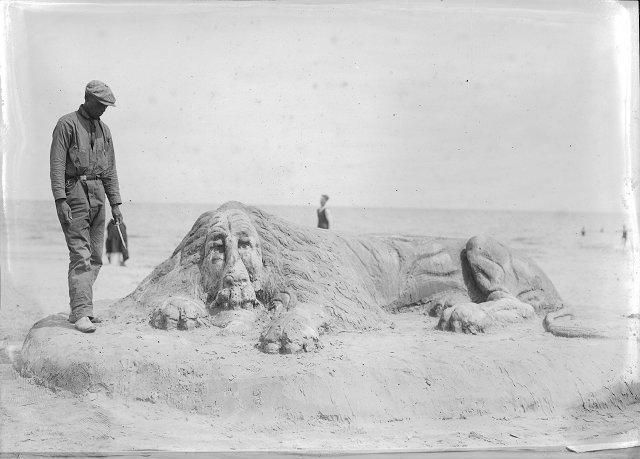 Robert Pernell stands next to a life-sized lion he has sculpted from sand in Charlotte. Printed in Rochester Herald, August 6, 1922.