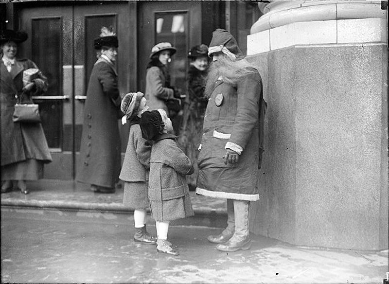 Two little girls have a chat with Santa in front of the Duffy-Powers Department Store on the corner of W. Main and Fitzhugh Streets, Rochester, NY. Printed in Rochester Herald, December 24, 1914. [PHOTO: Albert R. Stone collection]