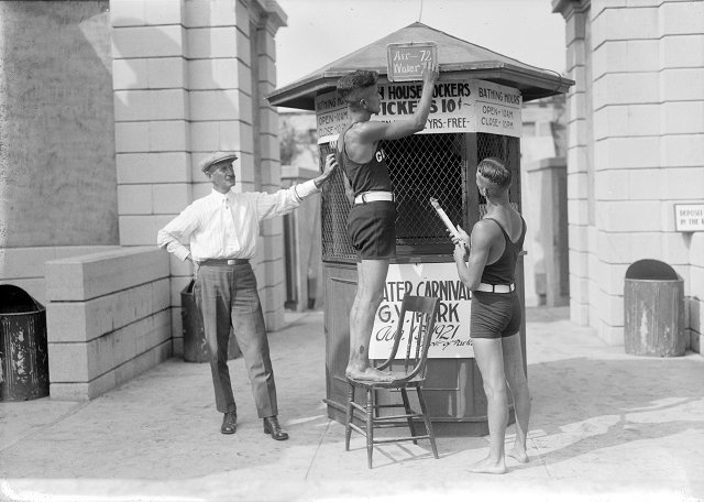 Frank Warren, ticket agent at the Durand-Eastman Park bathhouse, watches the lifeguards at work. Bud Martin and Roy Ackerman are writing the water and air temperatures on the chalkboard. August, 1921. [PHOTO: Albert R. Stone]