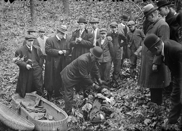 Detectives, men from the coroner's office, and bystanders gather around Francesco Manzello's dismembered body. It was found in a gully in Webster, packed into a whiskey barrel. The parts of the body had been folded up to fit into the barrel: his arms clasp his legs, which have been reversed, and his head rests on his arms and feet. [PHOTO: Albert R. Stone]