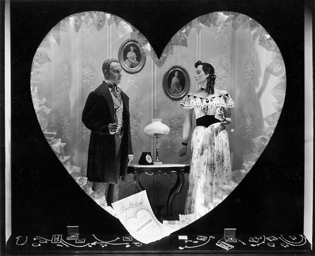 This scene was set up for Valentine's Day, and shows a Victorian era couple in a heart shape. A jewelry display is below them. c.1940. [PHOTO: Rochester Public Library]