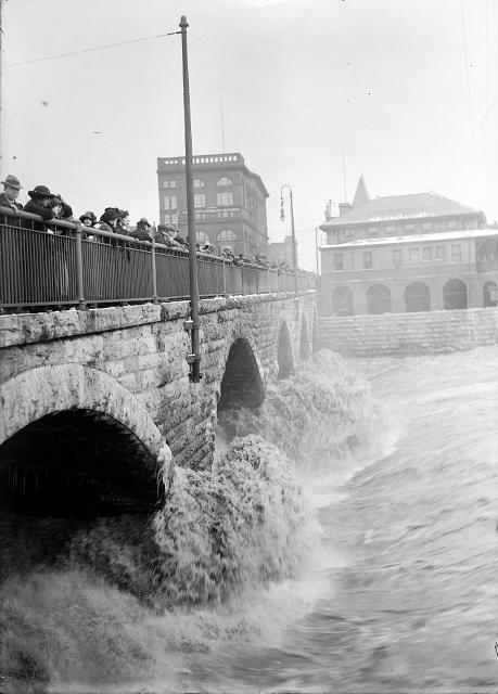 Spectators line the Court Street Bridge railings to watch flood waters beating against the arches of the bridge, below the dam. March, 1913. [IMAGE: Albert R. Stone]
