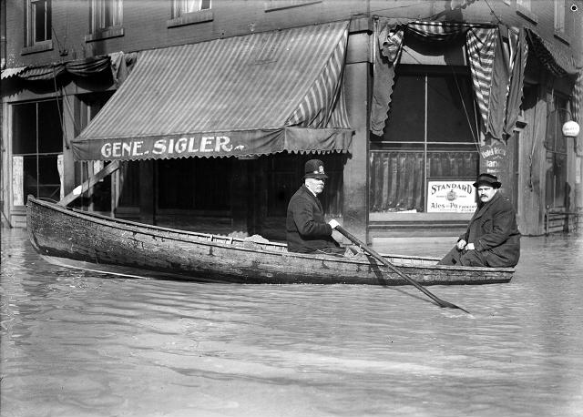 A Front Street policeman patrols his beat in a rowboat during the 1913 flood. He and another man row past the Hotel Richmond at the corner of Front and Market Streets. March, 1913. [IMAGE: Albert R. Stone]