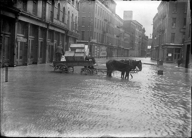 A horse and wagon stand in the middle of Mill Street during the 1913 flood. This is Mill Street at Andrews Street. Rochester Thread Company, F.A. Sherwood Company, John M. Forster Company, and Fahy Market are visible in the photo. March, 1913. [IMAGE: Albert R. Stone]