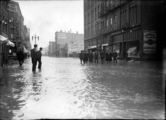 Men stand ankle deep in flood water on Front Street. They are in front of the Rochester Poultry & Commission Company. The People's Rescue Mission is in the background. March, 1913. [IMAGE: Albert R. Stone]