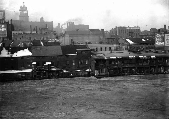 Genesee River in high water stage, showing the backs of Front Street buildings. This is believed to be a depiction of the flood of March 28, 1913. Myer's Department Store, Charles Adam (grinding), and Zweigle's (sausage maker and saloon) are visible in the photo. Weis & Fisher Company (furniture and carpets) is in the right background at 297 Brown Street. The Powers Building tower is in the upper left corner.  March, 1913. [IMAGE: Rochester Municipal Archives]