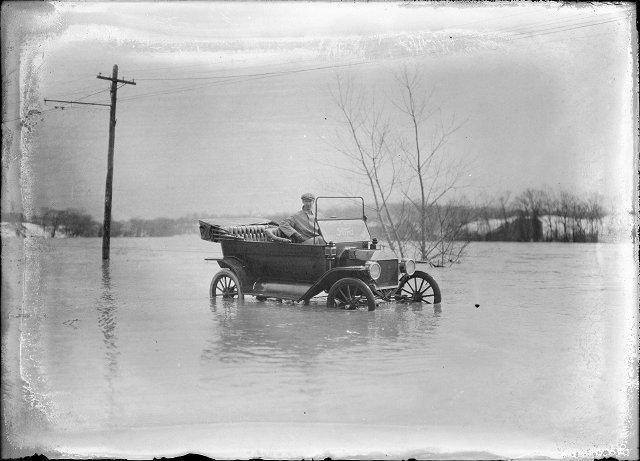 A man sits in a Ford automobile, which has water halfway up the wheels. This is Plymouth Avenue, which has been completely flooded by the Genesee River. March, 1913. [IMAGE: Albert R. Stone]