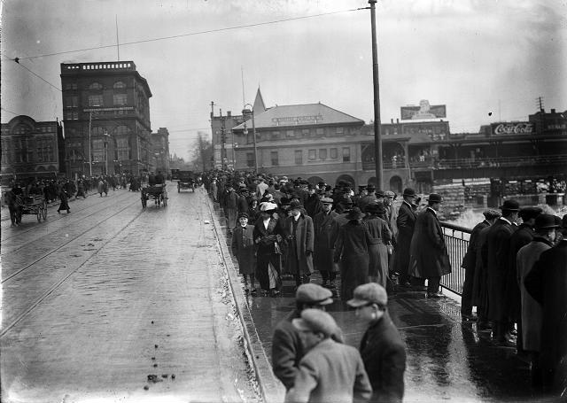 Pedestrians throng the sidewalks of the Court Street Bridge to see the flood waters, as a few horse-driven carriages and automobiles drive past. March, 1913. [IMAGE: Albert R. Stone]