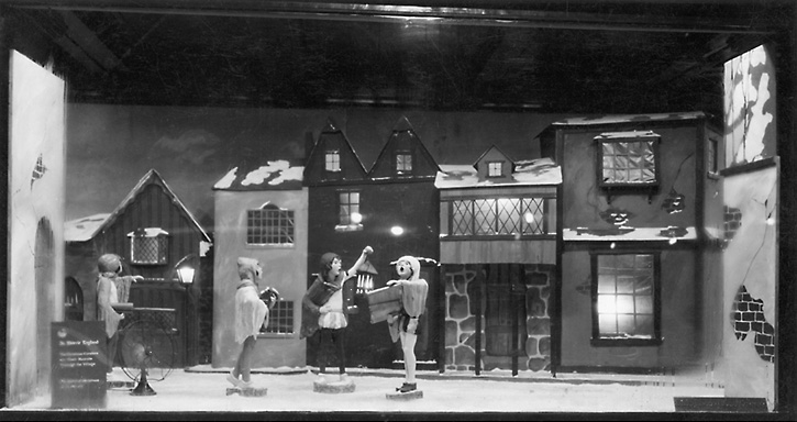 A Sibley's Christmas time window display with the theme of English carolers in a village. 'In Merrie England. The Christmas Carolers on Their Rounds Through the Village. The Spirit of Christmas in is in the air.' 1925. [PHOTO: Rochester Public Library]