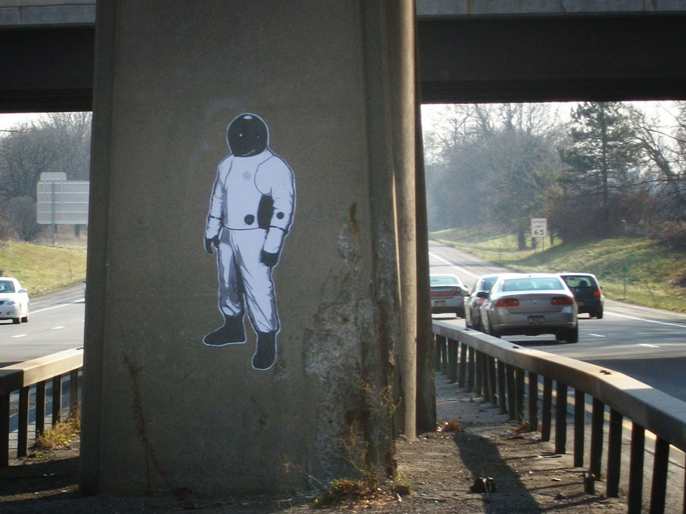 This Spaceman is stuck to a railroad bridge support column on I-490. He is facing eastbound traffic.