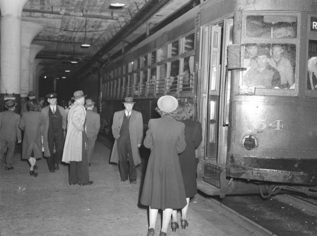A bustling subway station scene, showing people crowding the platform, and passengers lining up to leave the subway car. The scene is the underground City Hall station located at Broad and Exchange Streets. The eastbound car is heading for the end of the line at Rowlands. [Image from Rochester Municipal Archives]