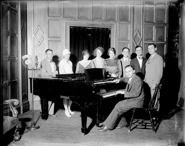 This group is gathered around a piano to perform for a WHAM radio broadcast (c.1927). The microphone is at far left. Identified are: 4th from left, Florence Knope Freeman; far right, Clayton Knope; at piano, James Quillian. [IMAGE: Albert R. Stone Negative Collection]