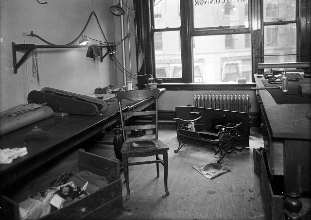 This was the Sibley Building office, and murder scene, of J. Frank O'Connor, a tailor merchant. A sewing machine and its table have been knocked over and lie in front of the radiator. The cutting table is at the right. A lower table, on the left, holds a bolt of fabric, a pressing board for sleeves, and an electric iron. A chair and a box of material sit in front of the lower table. [PHOTO: Albert R. Stone Collection]